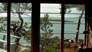A room with a large window overlooking a rocky coastline with trees.