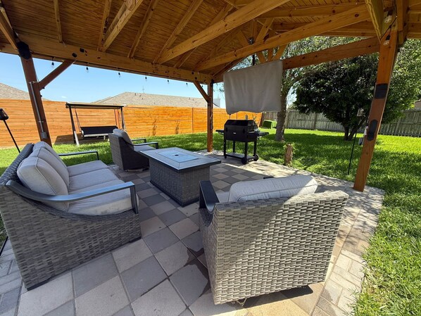 Un patio cubierto con mobiliario de mimbre, una parrilla y una mesa.