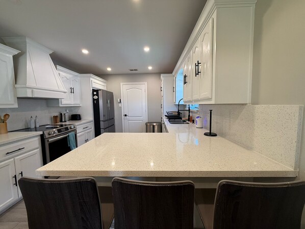 A modern kitchen with white cabinetry, a large island, and a stainless steel refrigerator.
