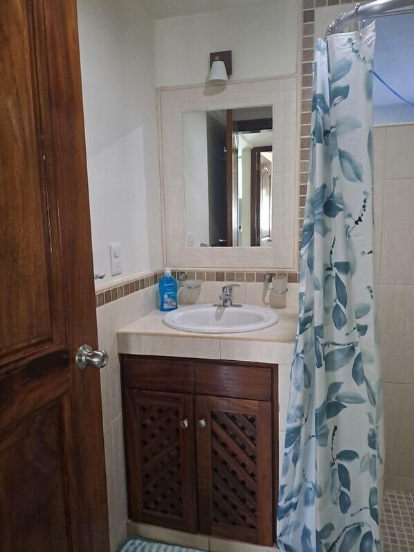 A bathroom with a wooden door, a white sink, a mirror, and a shower curtain with a leaf pattern.