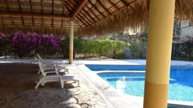 A pool area with a thatched roof, stone flooring, and white lounge chairs. - TERRAZAS BY YALP (Santa Maria Huatulco)