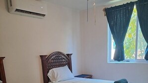 A bedroom with two single beds, a nightstand, a bedside table, an air conditioner, and a window with curtains. - TERRAZAS BY YALP (Santa Maria Huatulco)