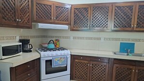 A kitchen with wooden cabinets, a white stove, a microwave, and a sink. - TERRAZAS BY YALP (Santa Maria Huatulco)