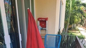 A balcony with a white table and two blue chairs, a red umbrella, and a red outdoor grill. - TERRAZAS BY YALP (Santa Maria Huatulco)