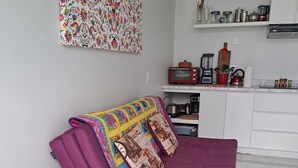 A modern living room with a purple sofa, a colorful quilt, and a small round table with a green coaster.