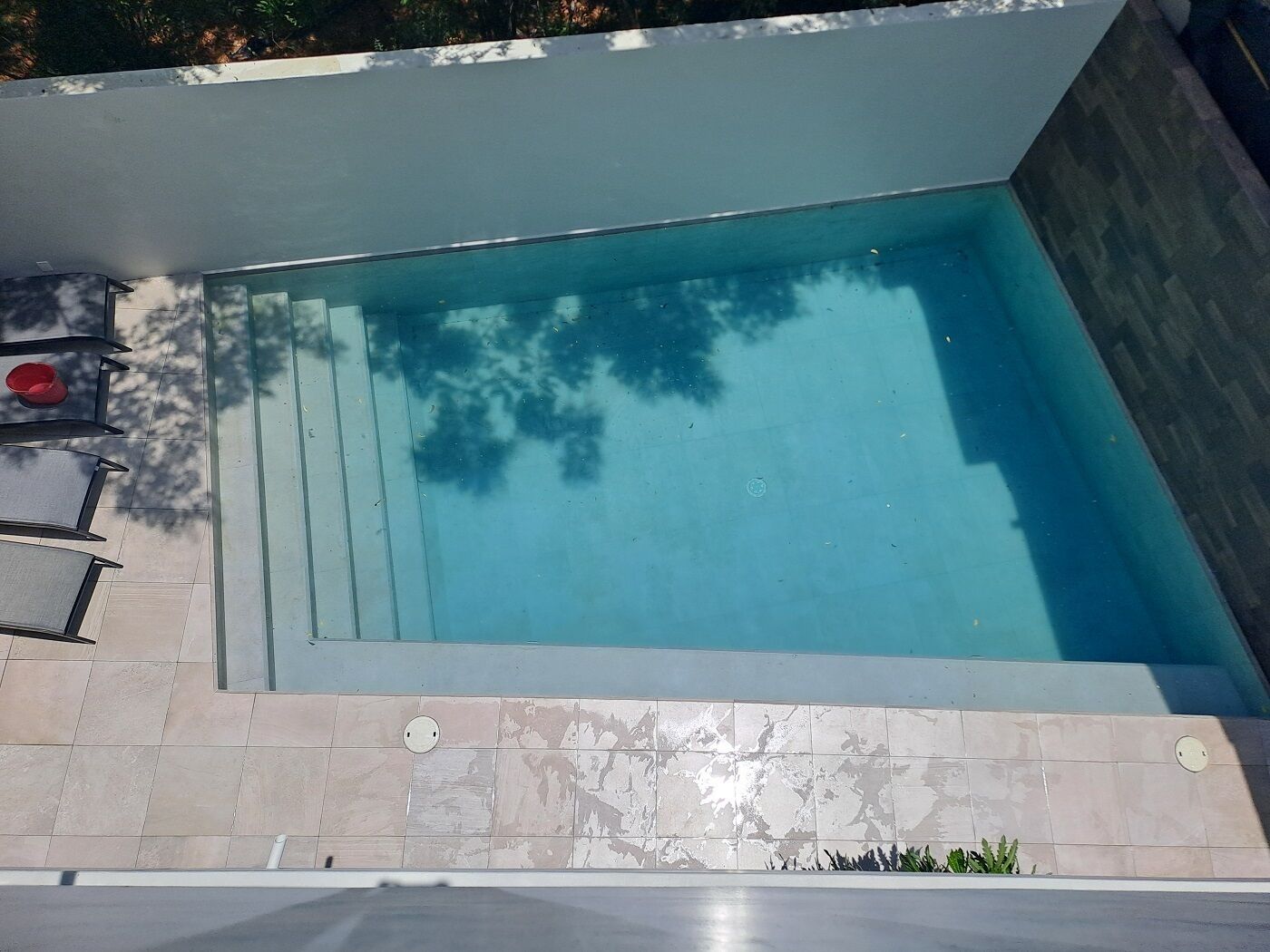 A rectangular swimming pool with a tiled deck and steps leading into it.