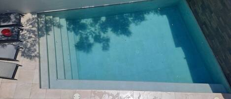 A rectangular swimming pool with a tiled deck and steps leading into it.