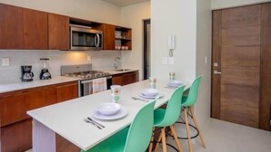 A modern kitchen with wooden cabinets, a microwave, and a dining area with a white table and green chairs. - XCAANDA BY YALP (Santa Maria Huatulco)