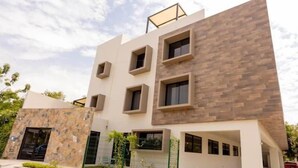 A modern multi-story building with a flat roof, rectangular windows, and a stone facade. - XCAANDA BY YALP (Santa Maria Huatulco)