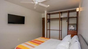 A bedroom with a bed, a ceiling fan, a TV mounted on the wall, and a wooden wardrobe with shelves. - XCAANDA BY YALP (Santa Maria Huatulco)
