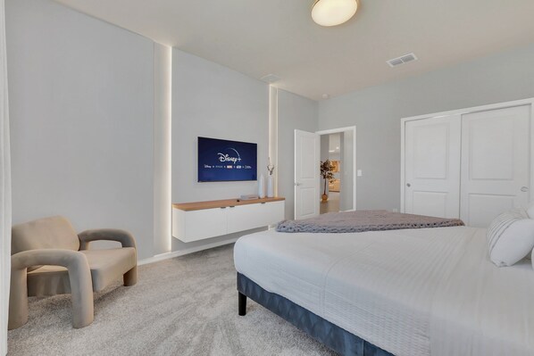 A bedroom with a bed, a chair, a TV mounted on the wall, and a door leading to another room. - EV_15985 - 10BR / 8BA Luxury Estate w/ Private Pool, Theater, Games Room (Clermont)