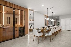 A modern dining area with a long table, white chairs, and pendant lighting.