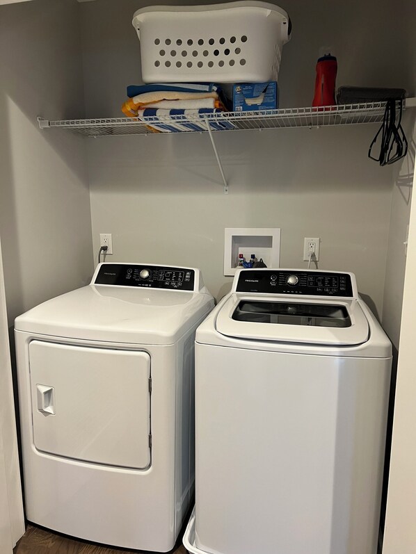 A laundry area with two front-loading washers and a shelf above containing folded towels and a water bottle. - Sunsets at Angola on the Lake Charming 3-bedroom townhome (Angola)