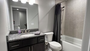 Un baño moderno con encimera de granito, inodoro blanco, bañera y cortina de ducha.