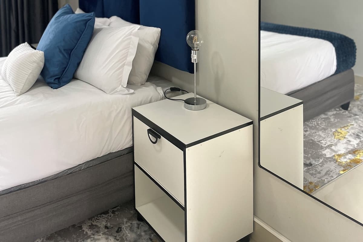 A neatly arranged bedroom with a bed, bedside table, and a mirror reflecting the room.