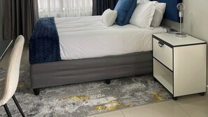 A neatly arranged hotel room with a bed, bedside table, and a chair. - 36 On Blougom (Midrand)