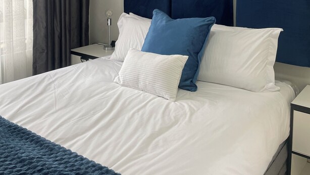 A neatly made bed with white and blue pillows, a dark blue headboard, and a white bedside table with a lamp. - 36 On Blougom (Midrand)