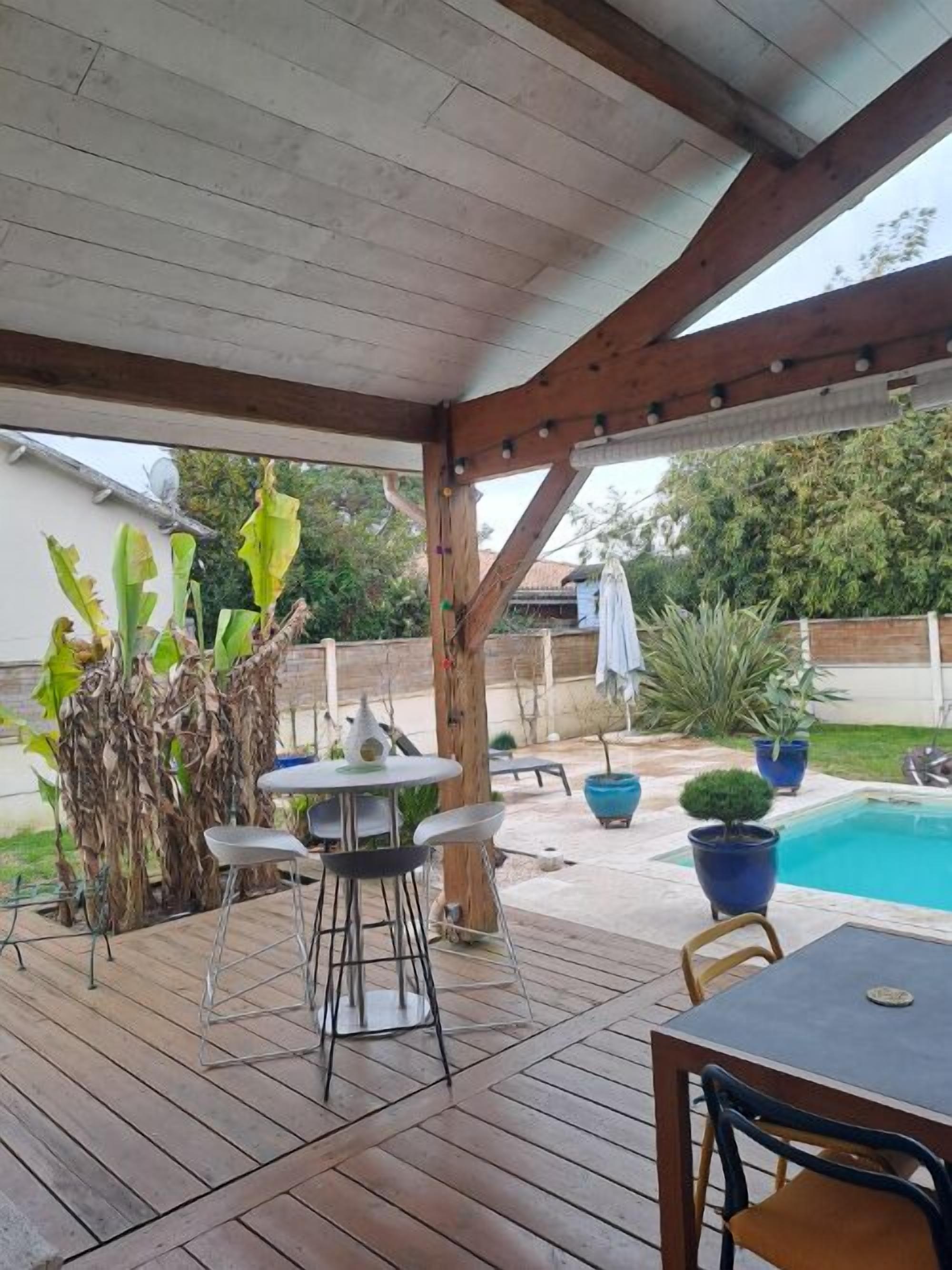 A covered patio area with a pool, wooden deck, and outdoor furniture.