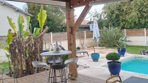 A covered patio area with a pool, wooden deck, and outdoor furniture. - Jolie maison avec piscine (La Teste-de-Buch)