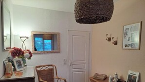 A room with a wicker chair, a small table with a picture frame, a mirror, and a door. - Jolie maison avec piscine (La Teste-de-Buch)