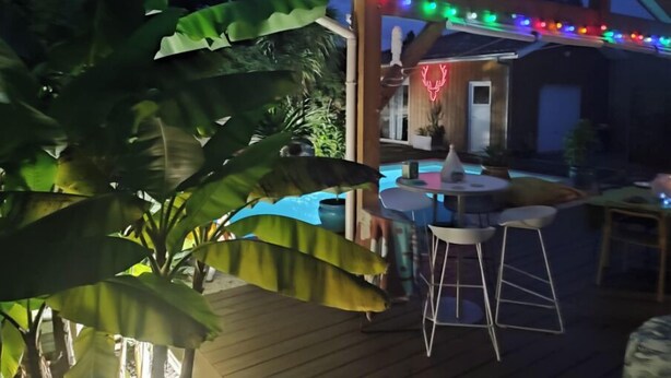A wooden deck with a pool, outdoor seating, and string lights. - Jolie maison avec piscine (La Teste-de-Buch)