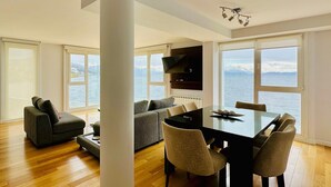 A modern living room with a dining area, large windows, and a view of the sea. - Oasis apartment on the Nahuel Huapi Lake (San Carlos de Bariloche)