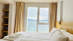 A hotel room with a large bed, a bookshelf, and a view of the sea through a window. - Oasis apartment on the Nahuel Huapi Lake (San Carlos de Bariloche)