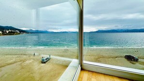 A view of a beach with a car parked on the shore, a person walking, and mountains in the background. - Oasis apartment on the Nahuel Huapi Lake (San Carlos de Bariloche)