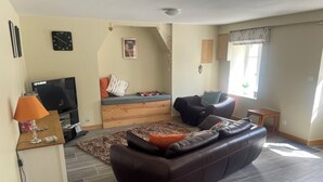 A living room with a brown leather sofa, a wooden coffee table, a TV, and a small table with a lamp.