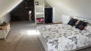 A bedroom with a large bed, a wooden desk, a bookshelf, and a stone wall.