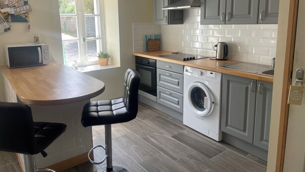 A compact kitchen with grey cabinets, a built-in oven, a microwave, and a washing machine.