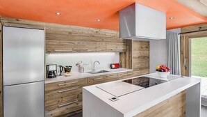 A modern kitchen with a central island, built-in appliances, and a wooden accent wall. - Chalet, 200m from ski slopes, terrace, balcony, fireplace or stove, parking, tv, ski locker, 200m² (La Clusaz)