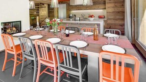 A modern dining area with a long table set for six, surrounded by orange and gray chairs. - Chalet, 200m from ski slopes, terrace, balcony, fireplace or stove, parking, tv, ski locker, 200m² (La Clusaz)