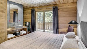 A wooden cabin bedroom with a large bed, a vanity with a mirror, and a view of the outdoors through a sliding door. - Chalet, 200m from ski slopes, terrace, balcony, fireplace or stove, parking, tv, ski locker, 200m² (La Clusaz)