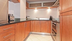 A kitchen with wooden cabinets, a stainless steel range hood, a built-in oven, and a window above the sink. - Heart of Canary Wharf. Stunning dock views. Close to all amenities. (London)