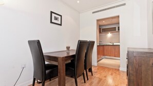 A dining area with a wooden table and four chairs, a framed picture on the wall, and a kitchen visible through an open doorway. - Heart of Canary Wharf. Stunning dock views. Close to all amenities. (London)