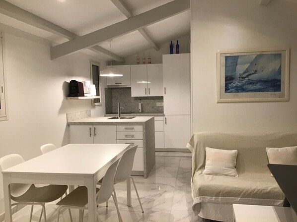 A modern kitchen with white cabinets, a dining table with chairs, and a sofa with cushions.