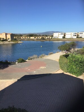 A residential area with a calm lake, paved pathways, and buildings in the background.