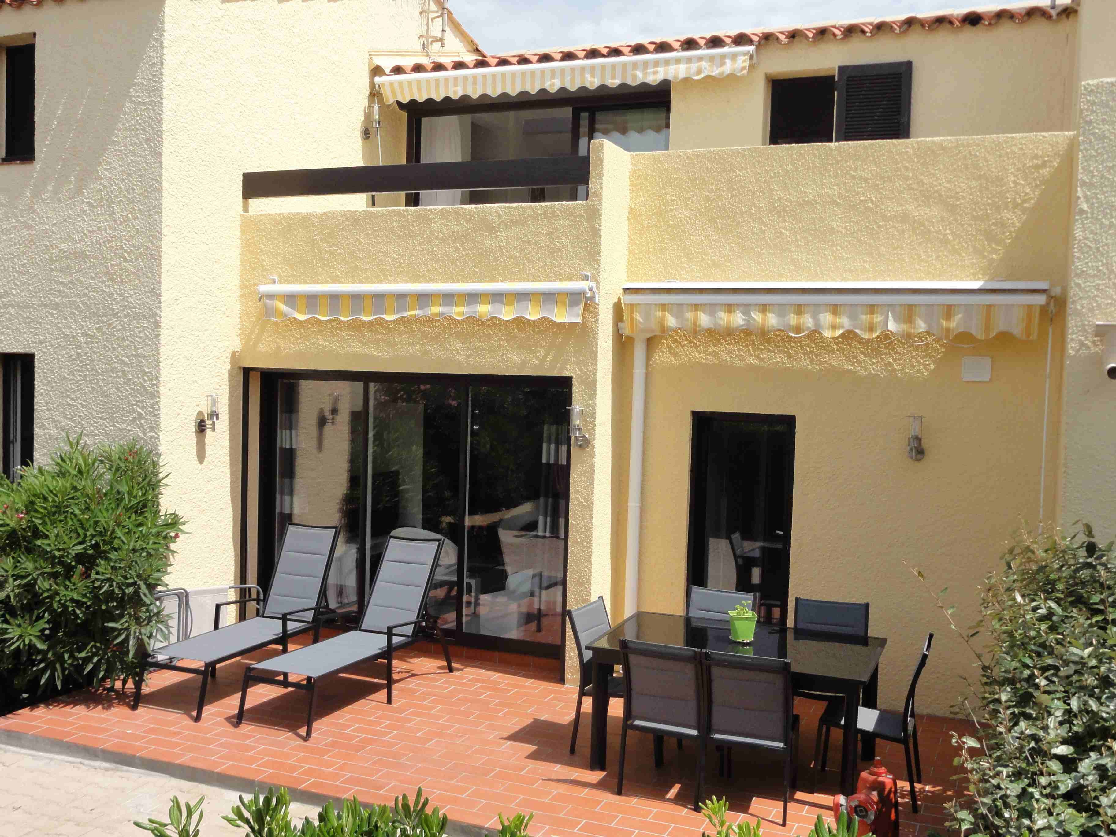 A two-story building with a patio area featuring a table and chairs, a small garden, and a red fire hydrant.