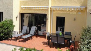 Ein zweistöckiges Gebäude mit einer Terrassenfläche, ausgestattet mit Tisch und Stühlen, einem kleinen Garten und einem roten Hydranten.