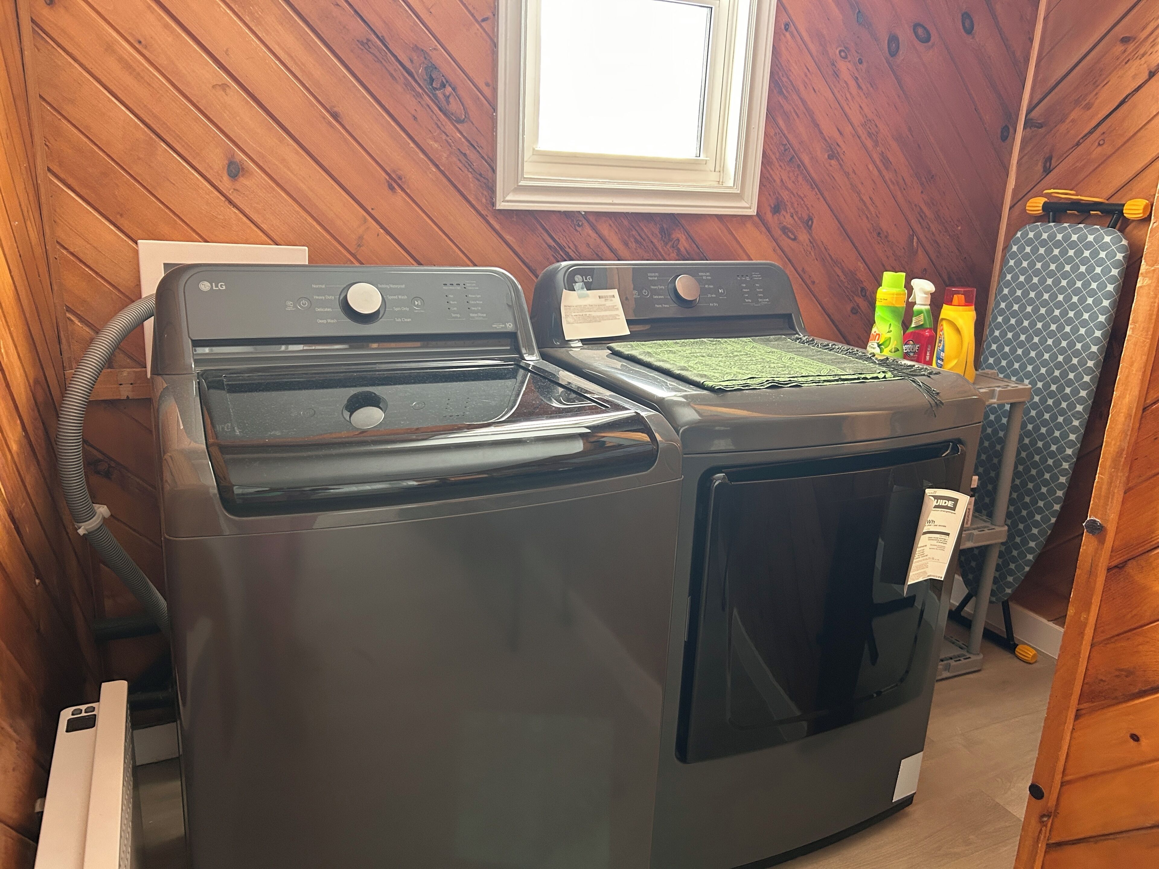 A laundry room with two stacked washers and dryers, wooden walls, a window, and cleaning supplies.