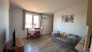 A living room with a sofa, a dining table with chairs, a television on a stand, and a fireplace painting on the wall. - 
Bridge View near Confederation Bridge and Beaches (Borden-Carleton)