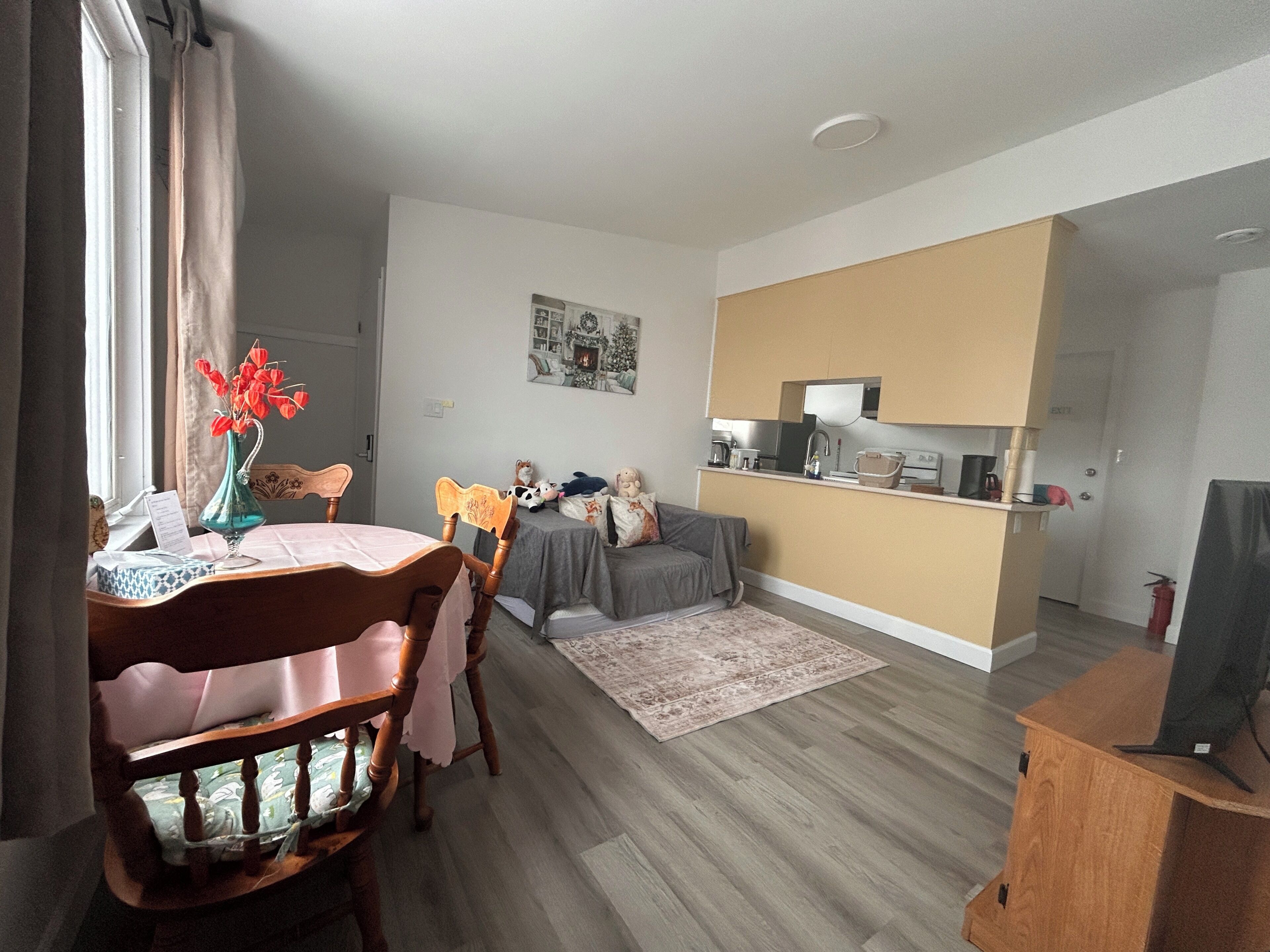 A modern living room with a dining area, a grey sofa, a small kitchen, and a wooden cabinet.