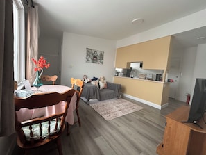A modern living room with a dining area, a grey sofa, a small kitchen, and a wooden cabinet.
