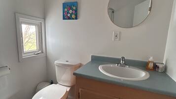 Een badkamer met toilet, wastafel, spiegel en een klein raam.