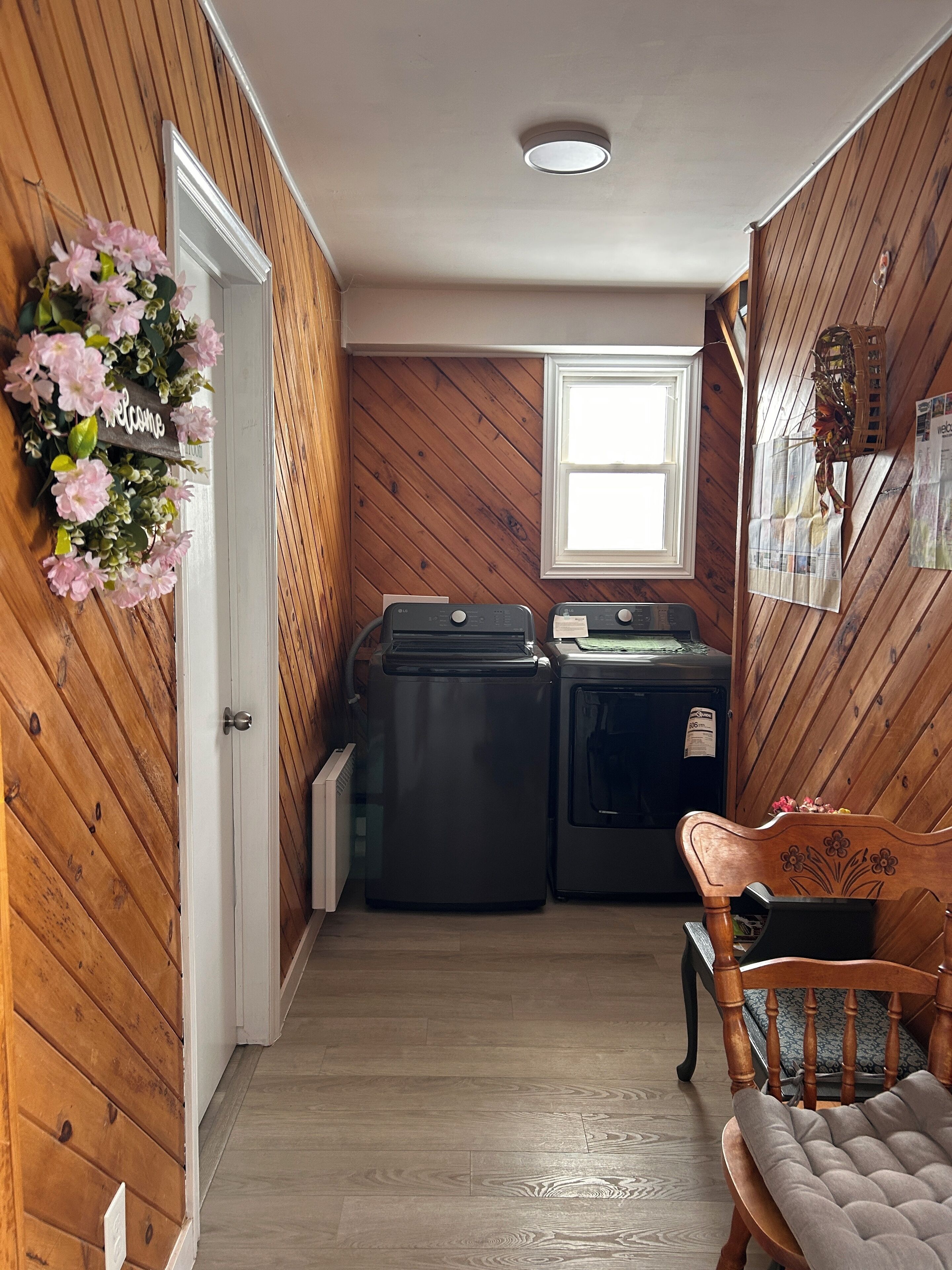 A laundry room with wooden walls, a white door, a window, and a chair.