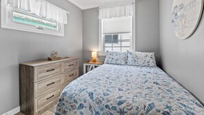 Un dormitori amb un llit, una petarrera, una làmpada i una finestra amb cortines.