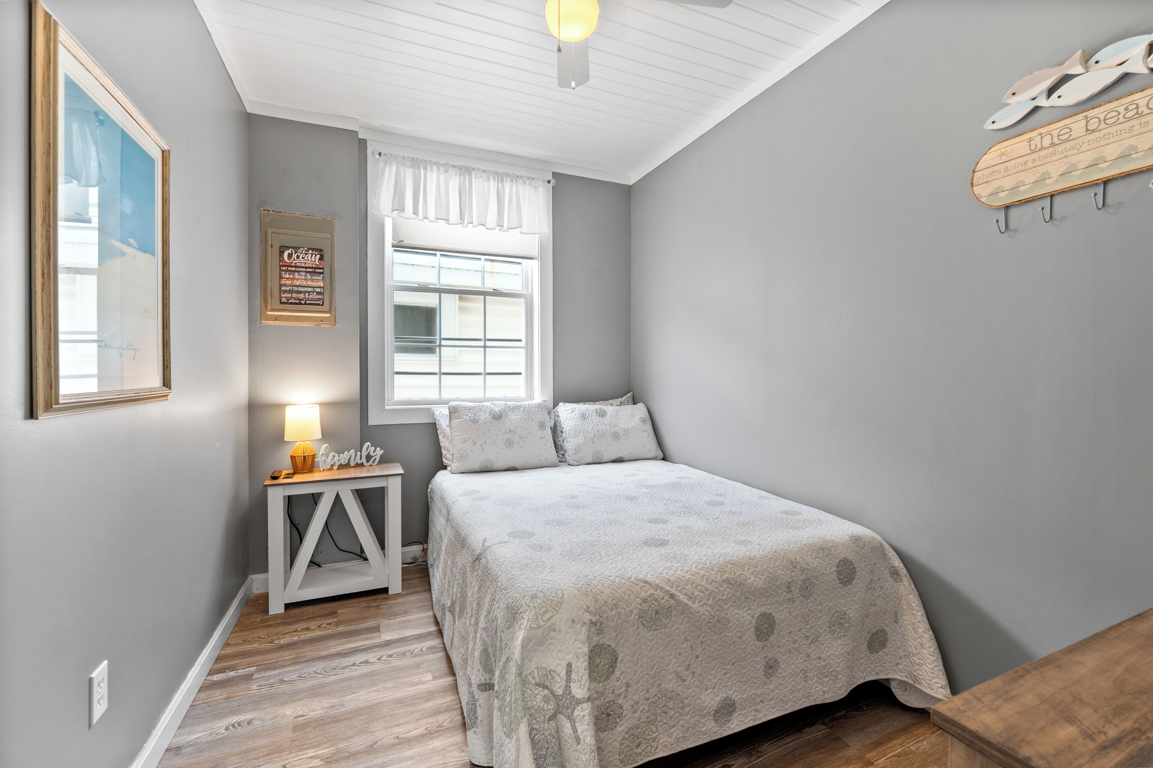 A bedroom with a bed, a nightstand, a window with curtains, a wall-mounted shelf, and a framed picture.
