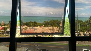 A view through a window of a coastal area with a beach, ocean, and a road with vehicles. - Edificio Neo Apto 401-Mandi H (Maceio)