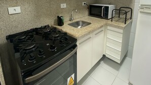 A kitchen with white cabinets, a gas stove, a microwave, and a sink. - Edificio Neo Apto 401-Mandi H (Maceio)